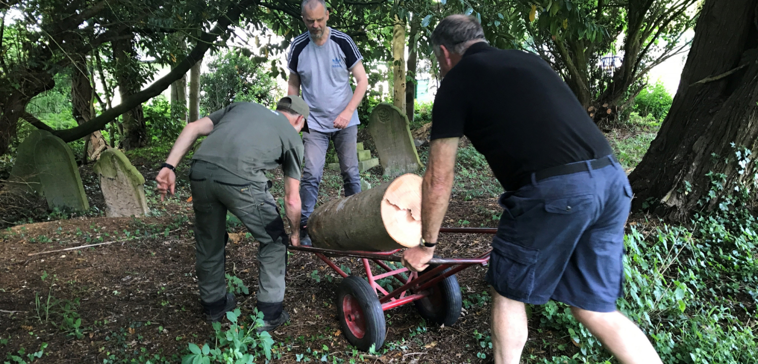 Men transporting logs in churchyard